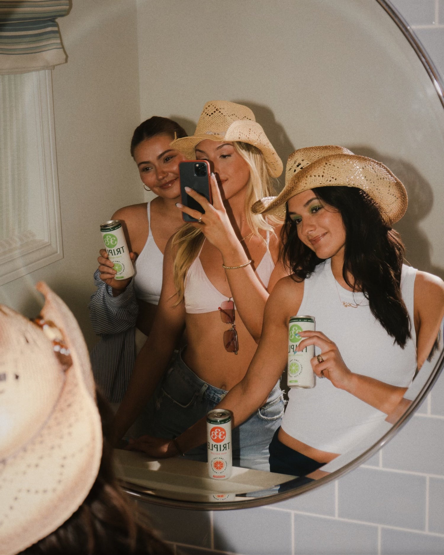 Three women taking a photo in a mirror posing with Triple THC seltzers